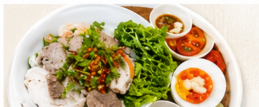 A bowl of Kuy Teav Phnom Penh with rice noodles, sliced pork and fresh herbs, served with lime, chili and condiments